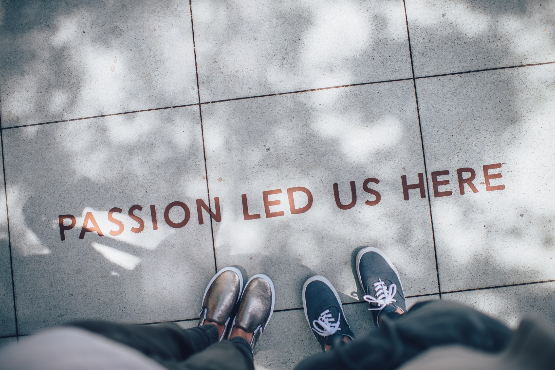 image of two sets of feet standing on a sidewalk with the words "Passion Led Us Here" printed on the sidewalk