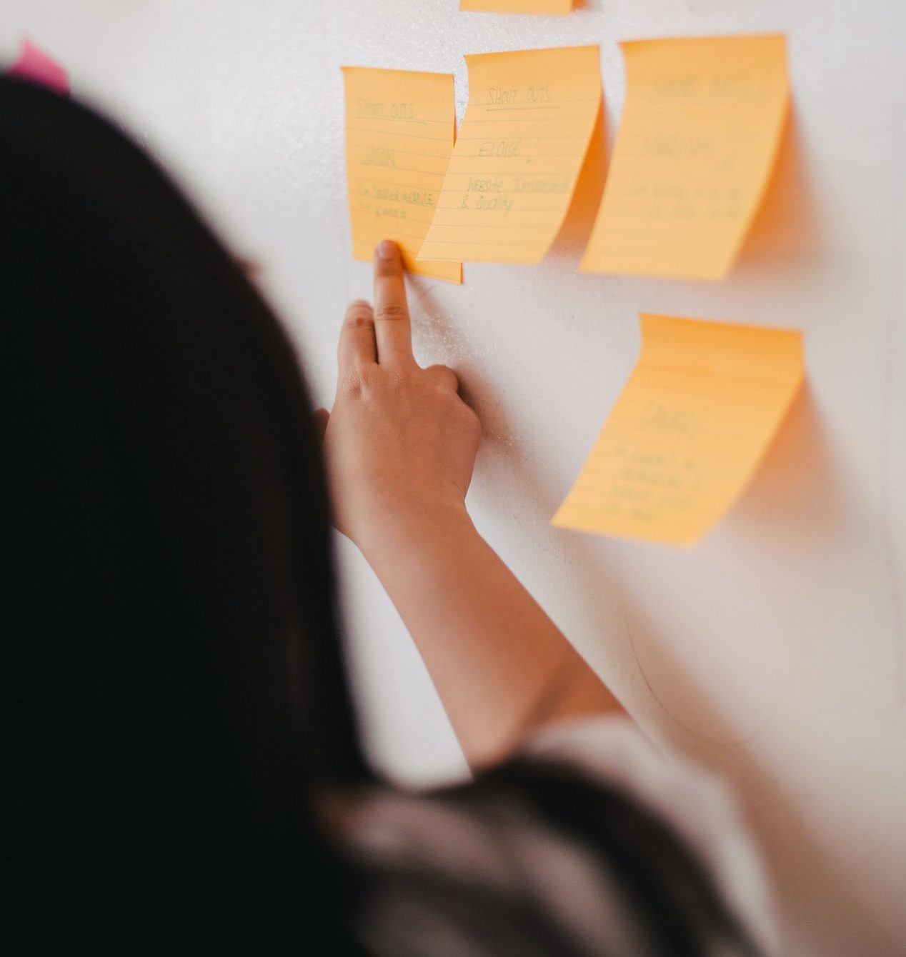 a person points to a collection of post-it notes on a wall