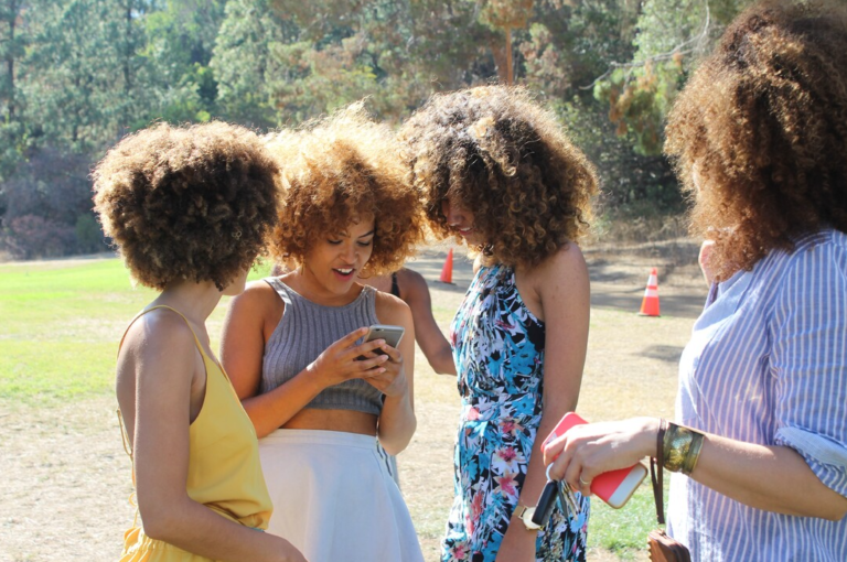 group of young girls at park gathered around a cellphone at a park