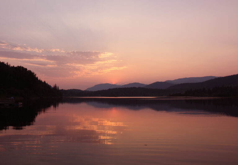 a lake with mountains in the background with a pink hue of sunset