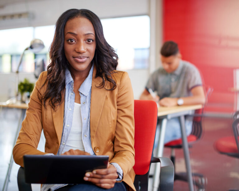 Confident Black female designer working on a digital tablet in red creative office space