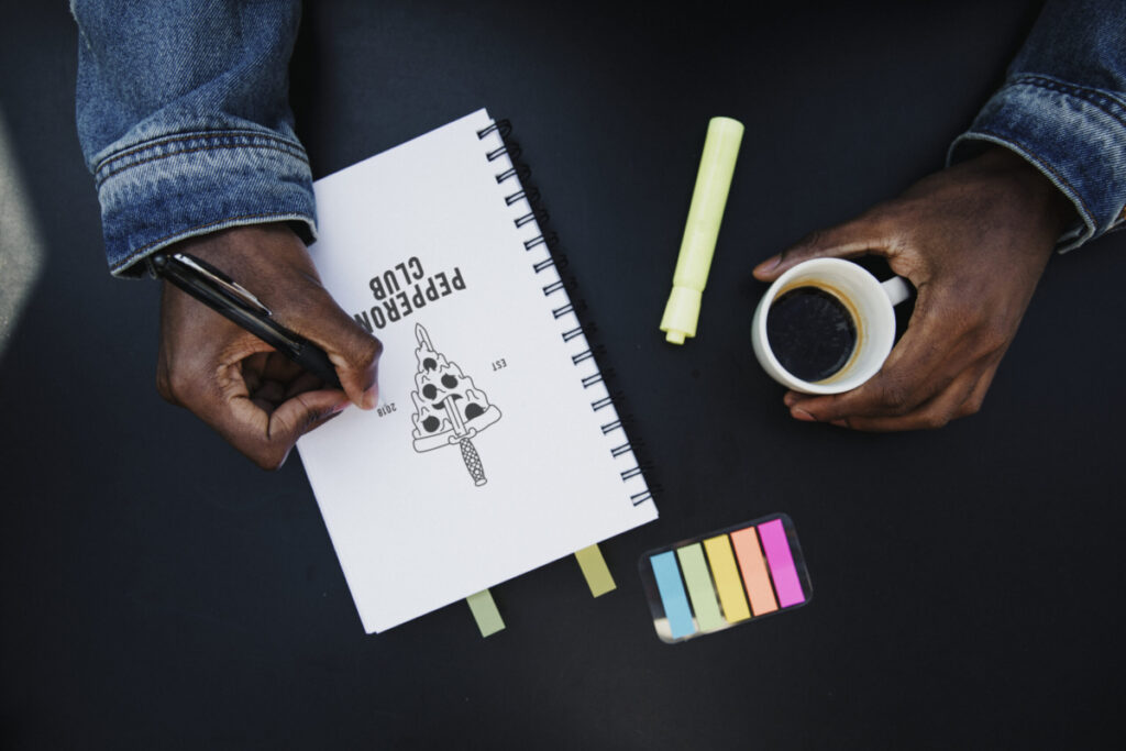 A Black man draws a logo on his notebook in a cafe