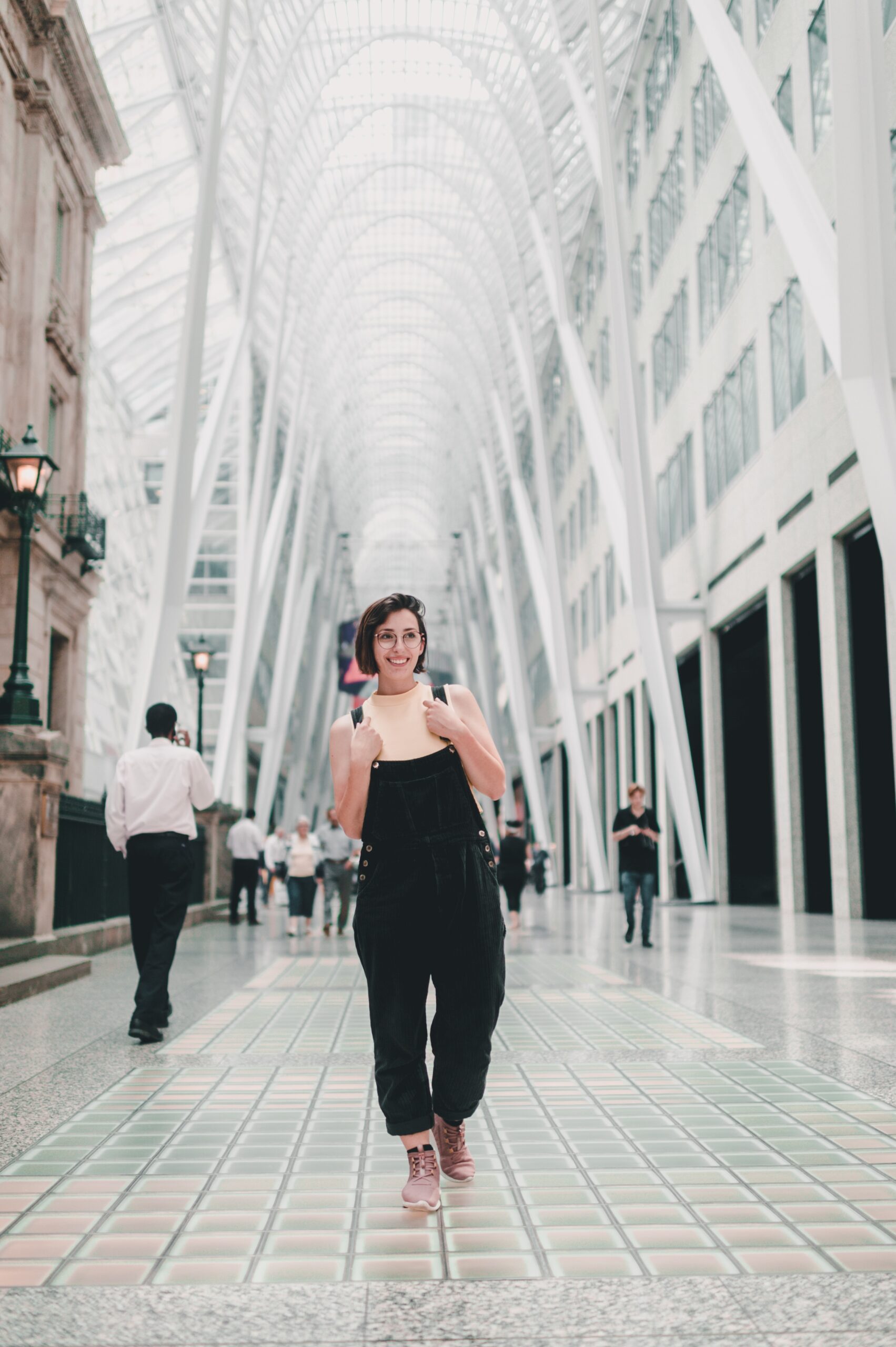 a young woman in black overalls walks through a concourse