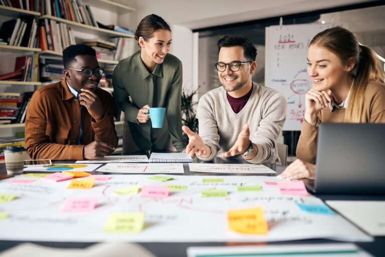 diverse group of young workers collaborate around poster with post-its