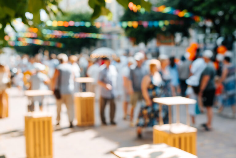 Defocused crowd of people at street festival in city walking along street decorated with multi-colored flags. Blurred abstract background of holiday and people on sunny summer day in park.