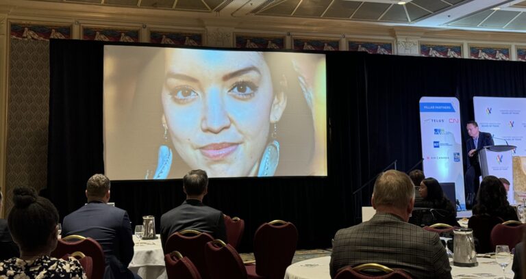 face of a young Indigenous woman on a screen in a hotel ballroom