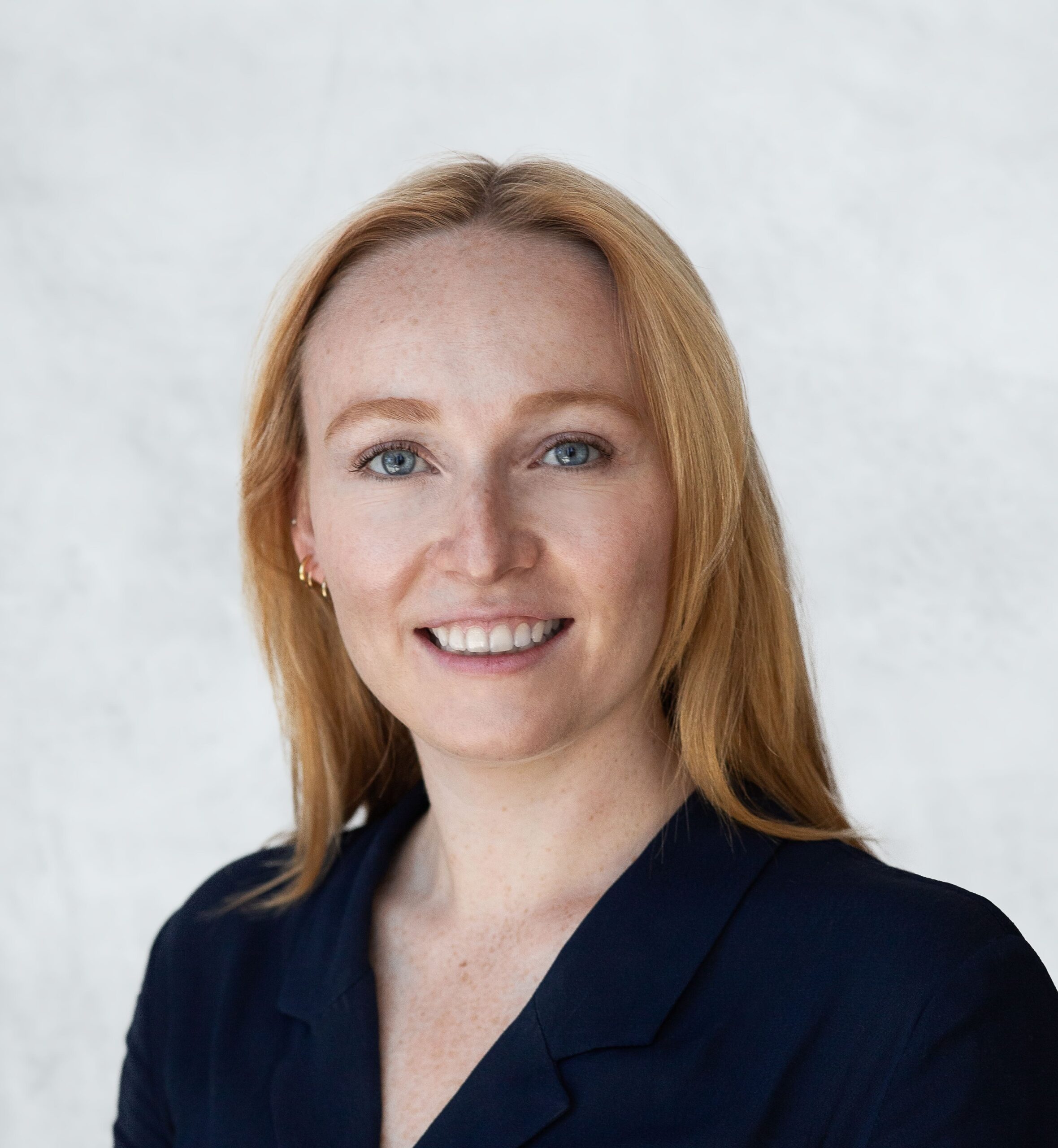 Caucasian woman with strawberry blonde hair and black blazer smiling in a corporate headshot