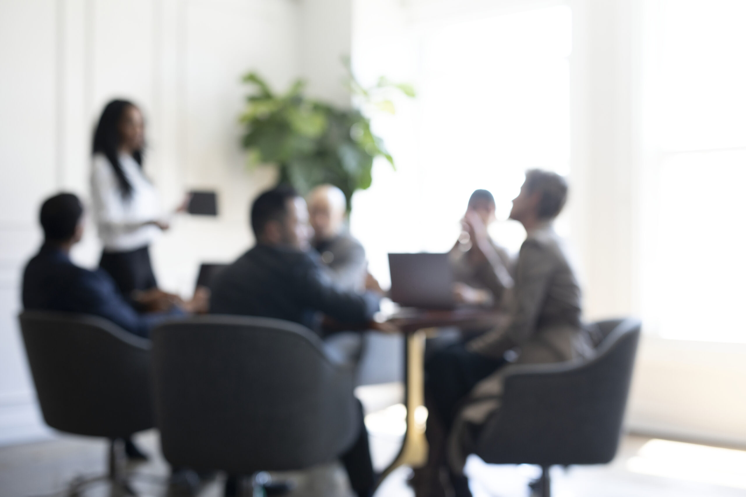 Blurred image of a group of people having a business meeting, one person standing to address the group