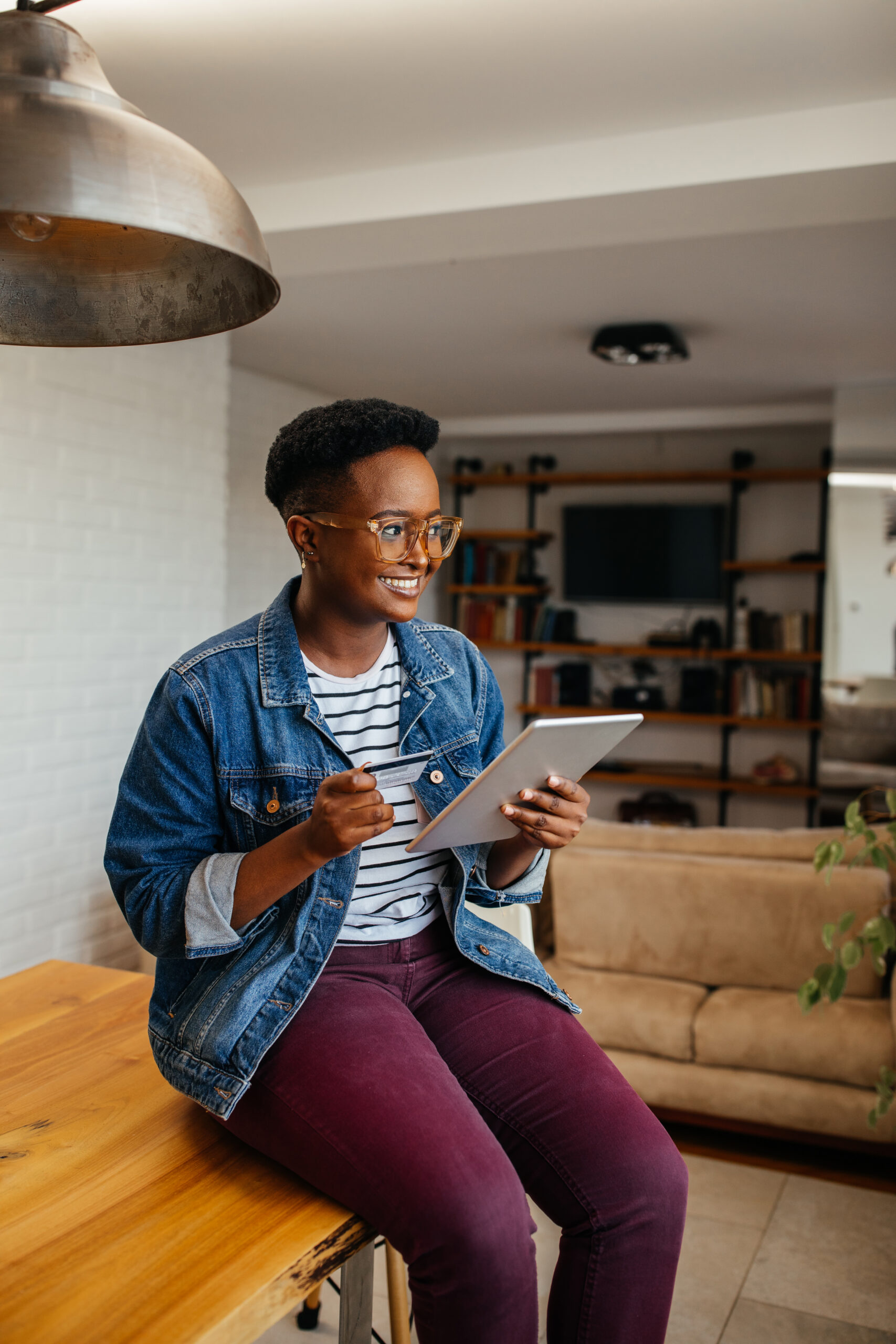 young black woman sits on table with ipad in her hand smiling