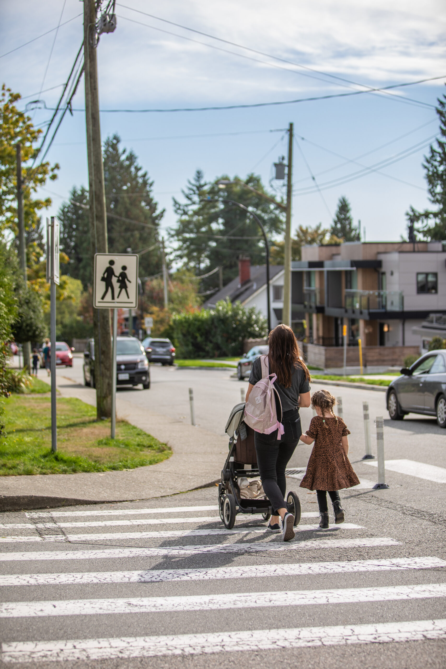 a mother finishes crossing a crosswalk pushing a stroller with a girl walking beside her