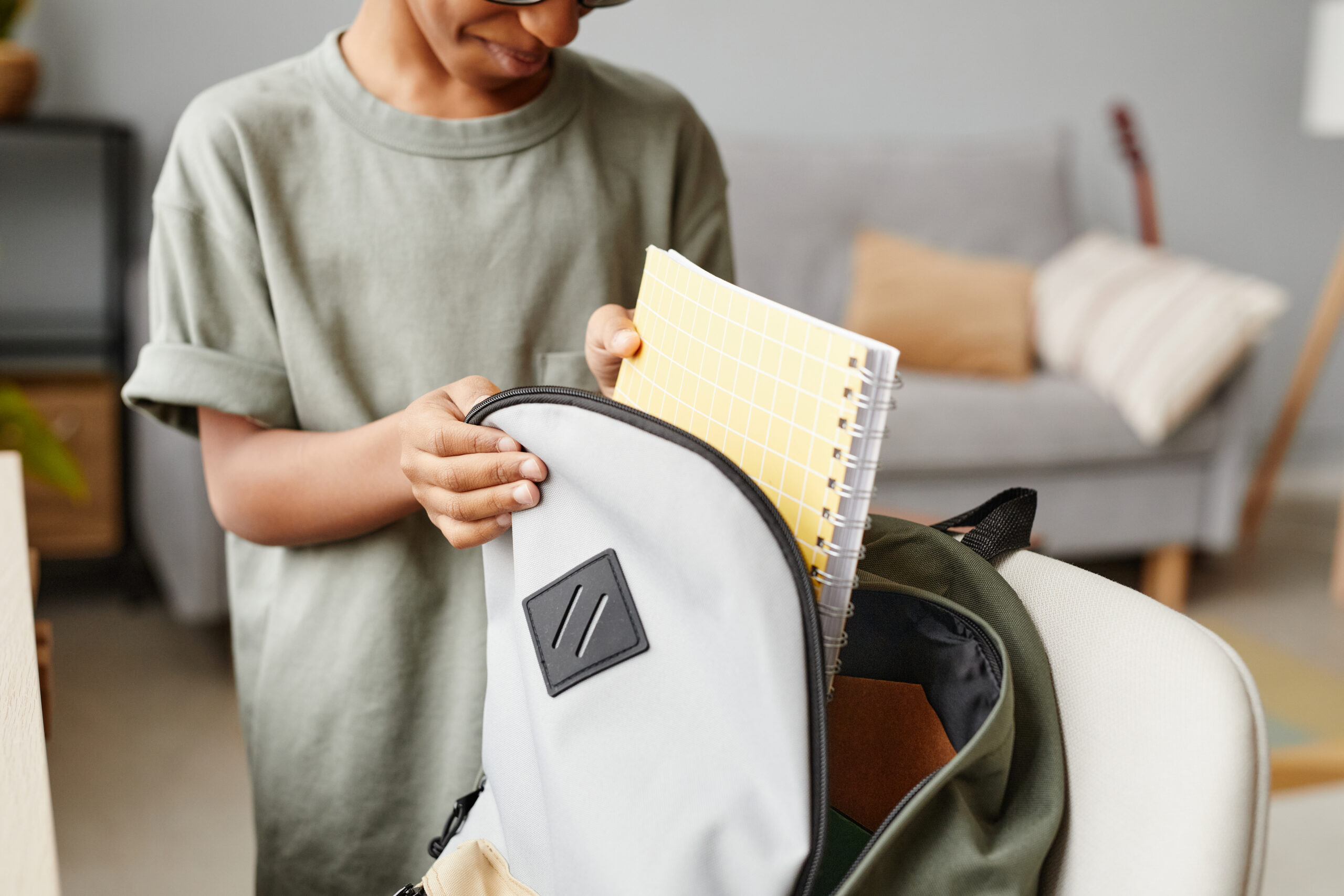 a boy in a grey shirt packs his backpack with a notebook